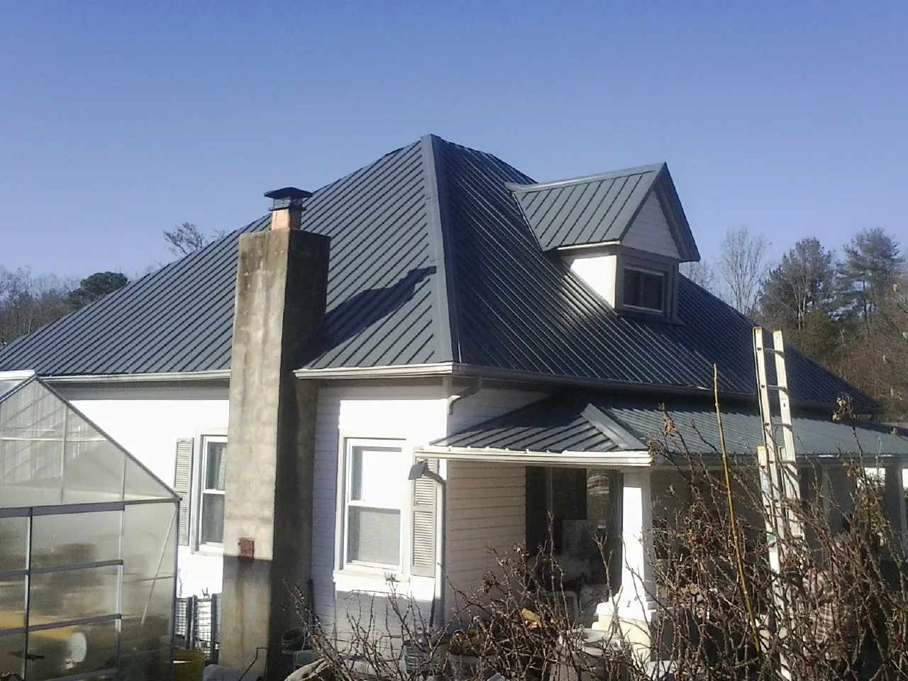 Dark blue standing seam metal roof on a white farmhouse with dormer — Slate & Tile Roof Repair by Roofing Brothers in Point Clear