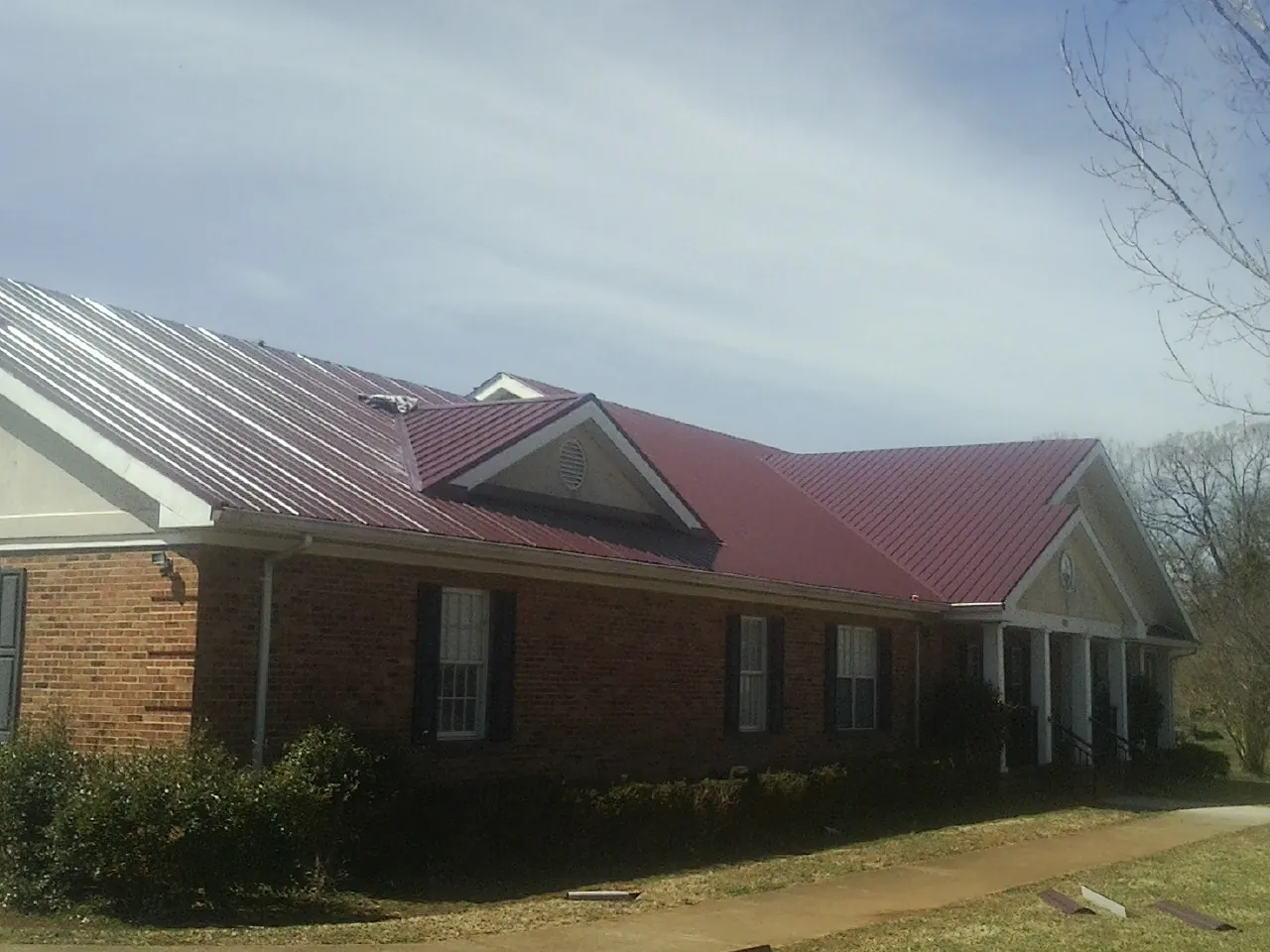 Red metal roof with gabled entries on a long brick building, from a Hail Damage Roof Repair job in Point Clear