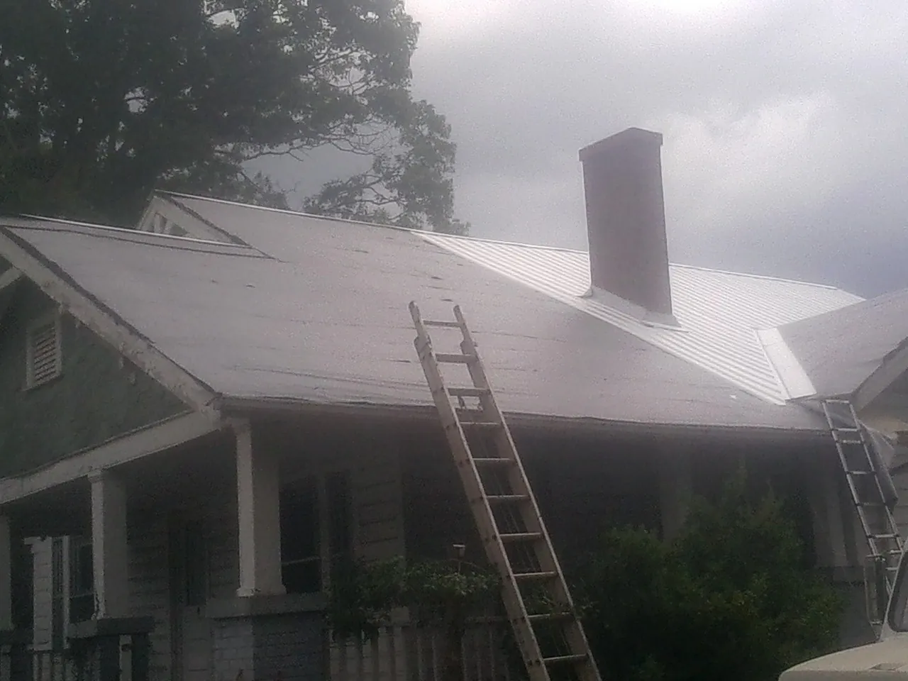 Ladders against a metal roof on an older home with a brick chimney in Point Clear