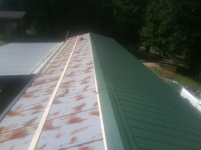 Old rusted panels beside newly installed green metal roofing — Wind Damage Roof Repair by Roofing Brothers in Point Clear