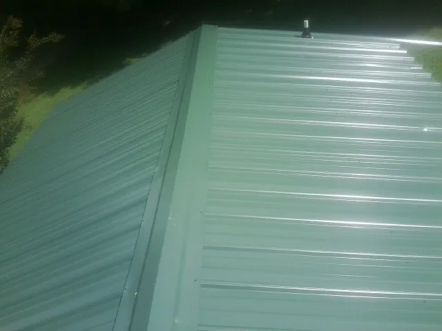 New green metal panels meeting at the ridge of a roof — Flat Roof Repair work by our crew in Point Clear