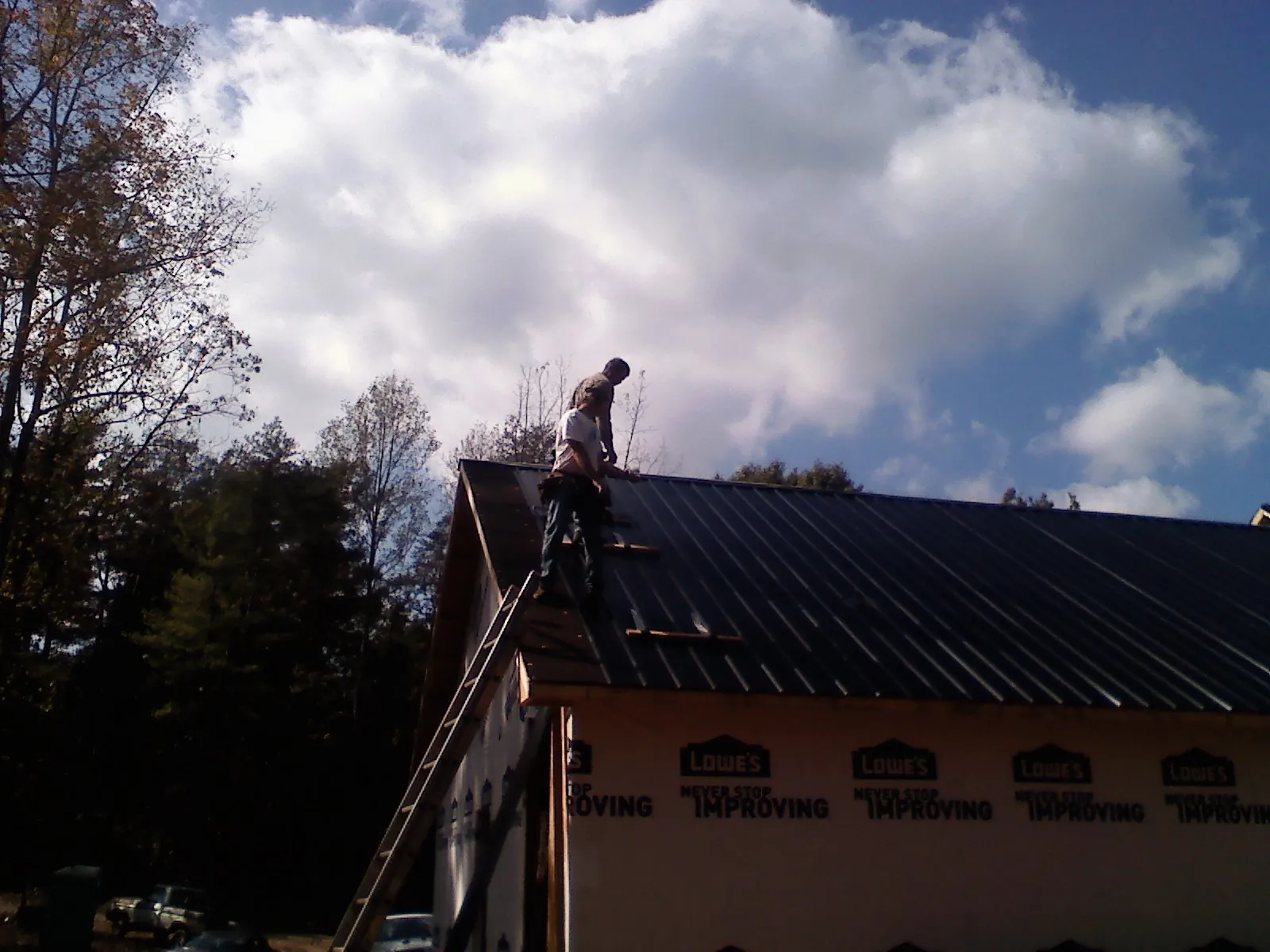 Roofer fastening dark metal panels high against a cloudy sky, from a Roof Inspection job in Point Clear