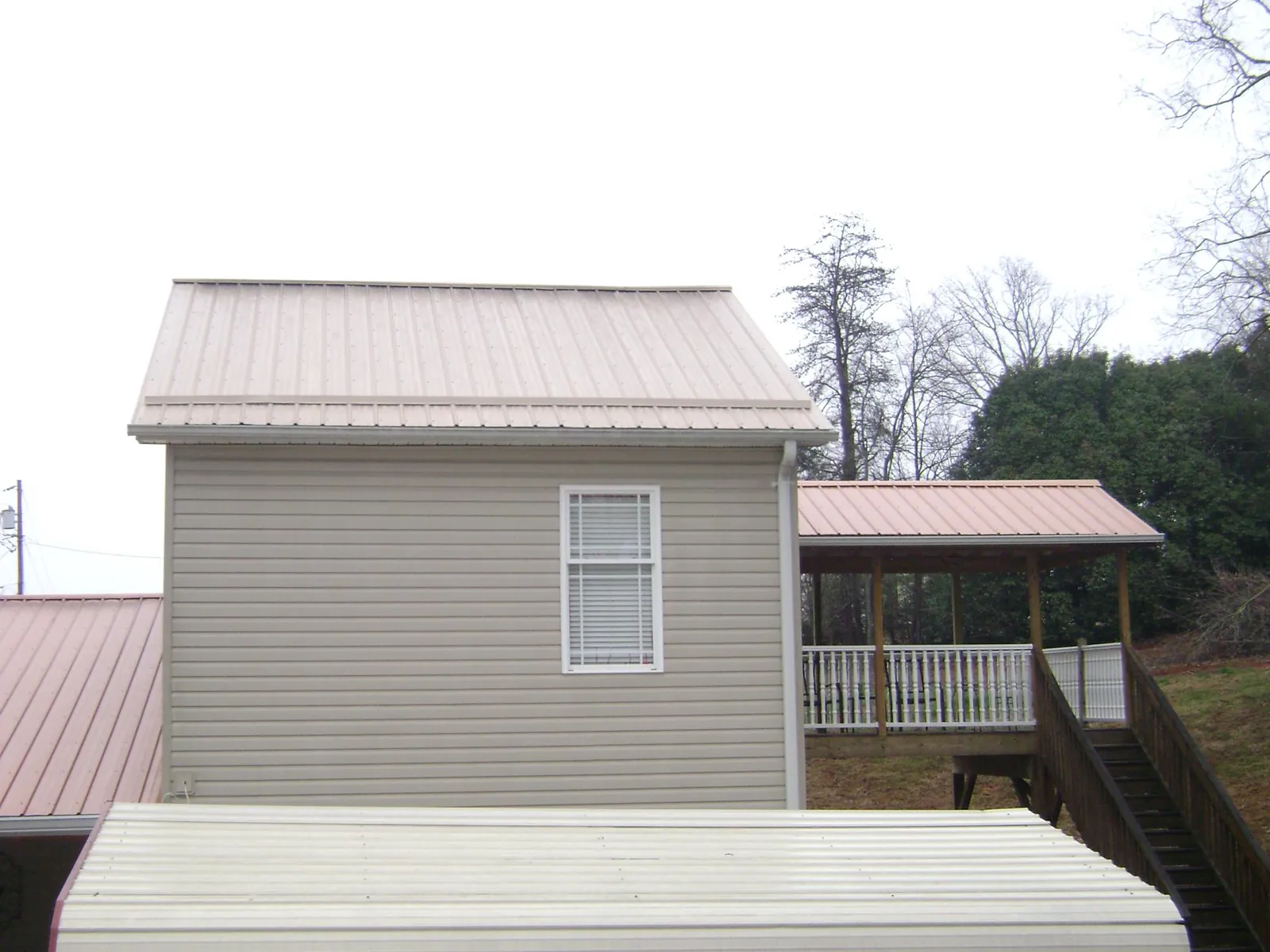 Tan metal roofs on a two story addition and attached porch, from a Roof Replacement job in Point Clear